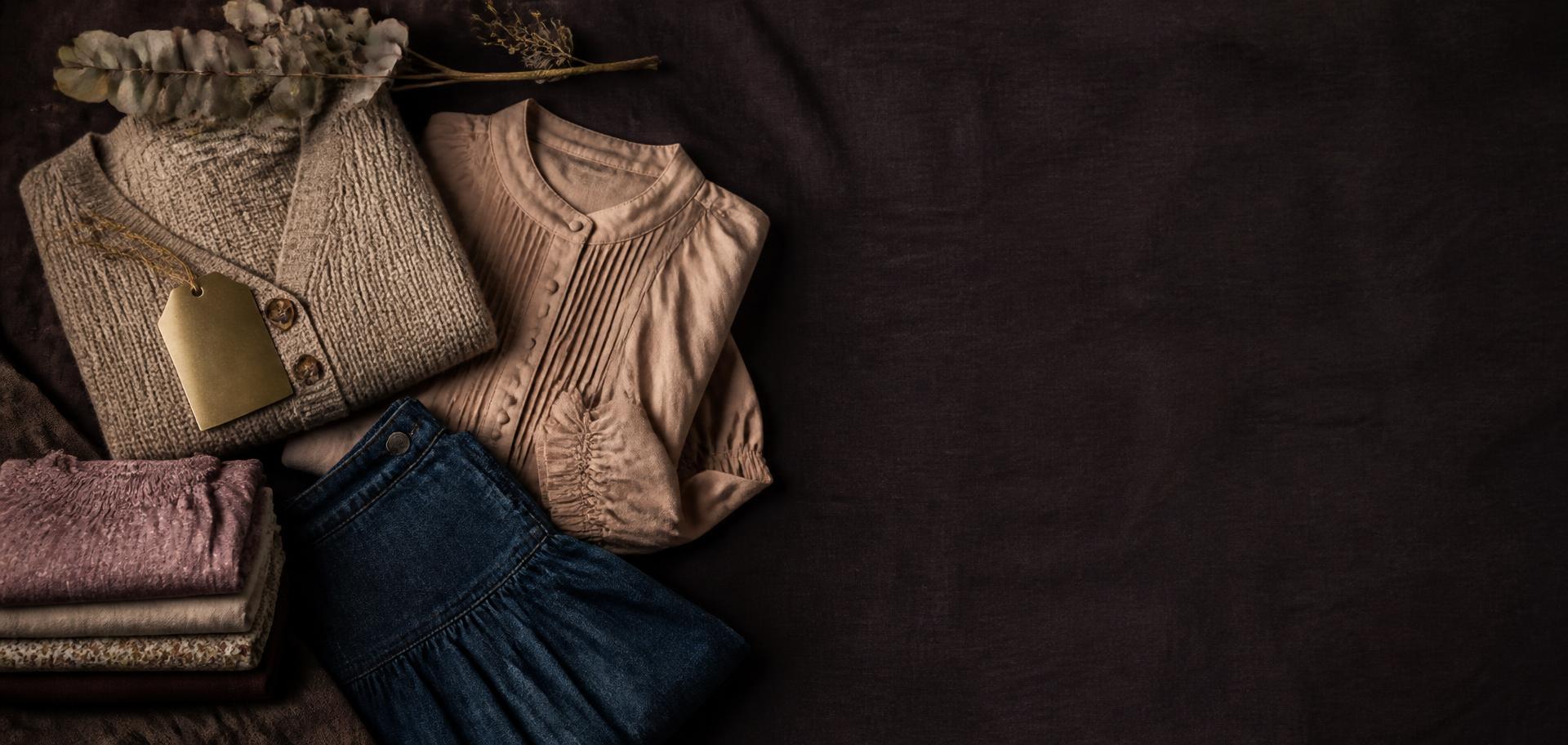 Outlet flat lay of folded neutral clothing on dark linen
